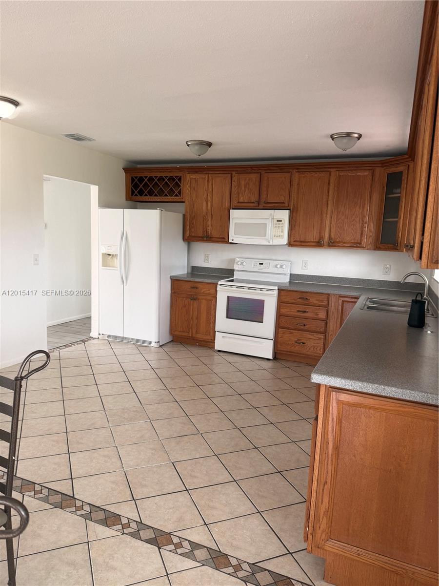 A kitchen features wood cabinets, white appliances, gray countertops, and diagonal tile flooring — 731 SW 24th St, Vero Beach FL 32962, VERO BEACH, FL