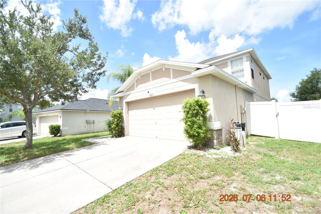 A two-story house with a beige stucco exterior, a two-car garage, and a white fence — 13556 FLADGATE MARK DRIVE, RIVERVIEW, FL