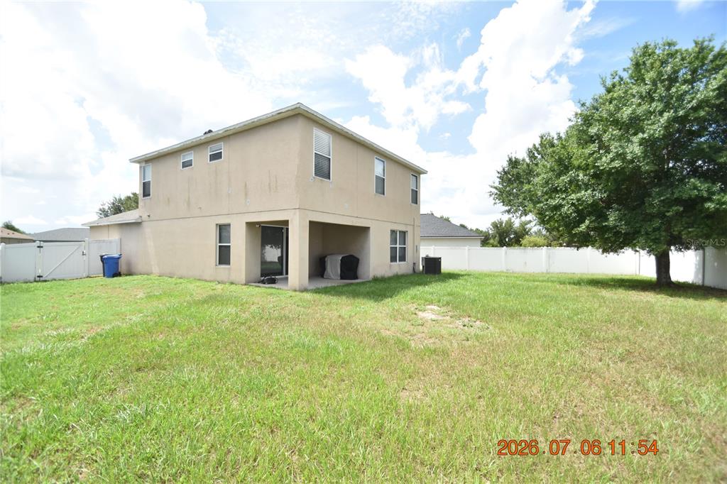 The rear exterior of a two-story stucco house features a covered patio and a fenced yard — 13556 FLADGATE MARK DRIVE, RIVERVIEW, FL