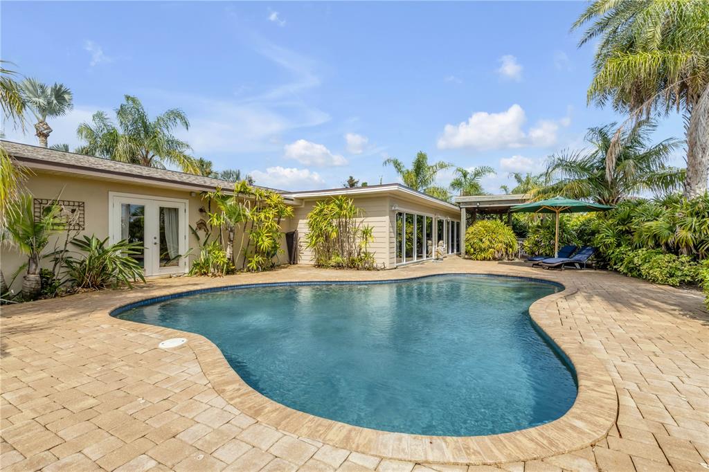 A kidney-shaped swimming pool sits on a paved patio beside a single-story house — 109 VIA BENEVENTO, NEW SMYRNA BEACH, FL