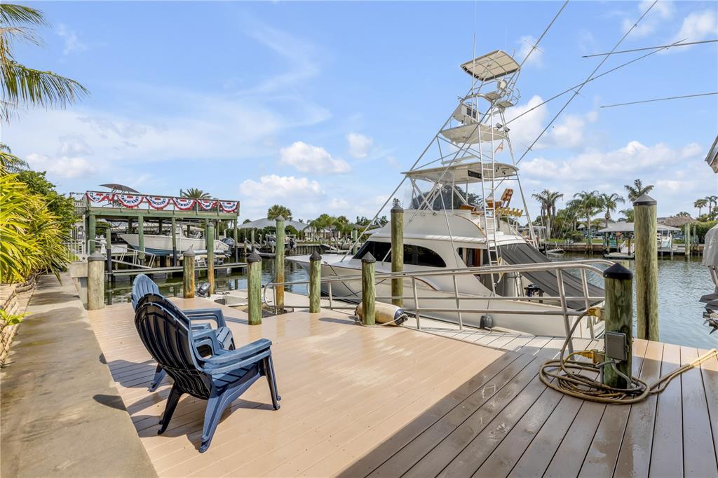 A wooden dock features two blue chairs overlooking a large boat in a canal — 109 VIA BENEVENTO, NEW SMYRNA BEACH, FL