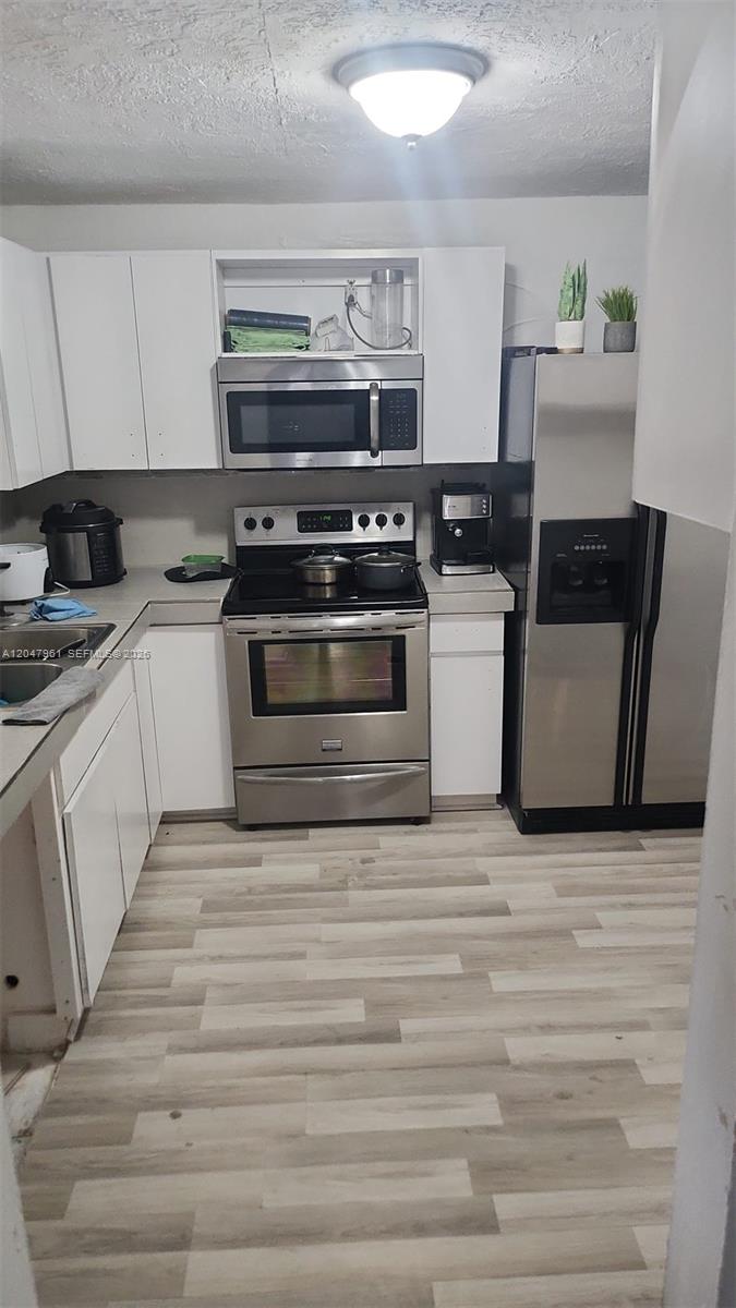 A kitchen features white cabinets, stainless steel appliances, and light-toned wood-look flooring — 15115 NE 6th Ave # 32, Miami FL 33162, MIAMI, FL