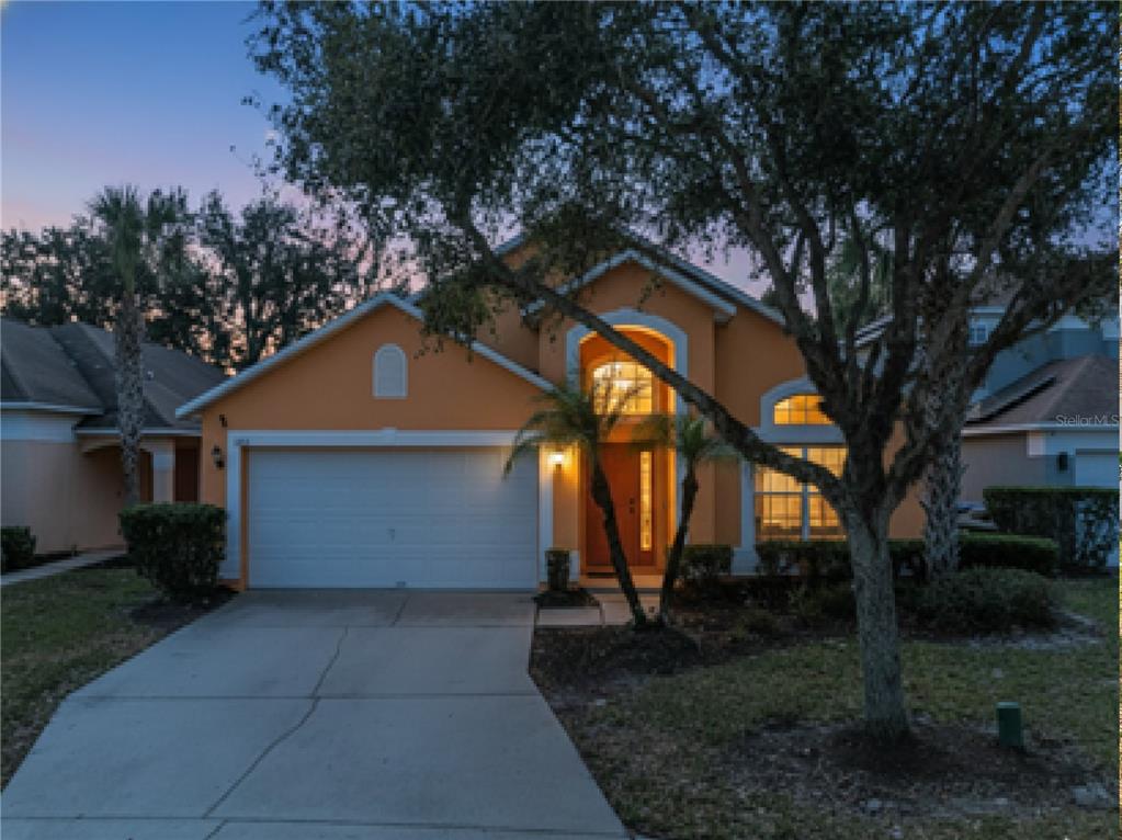 A one-story orange house with a two-car garage and a large tree in front — 1105 SEASONS BOULEVARD, KISSIMMEE, FL