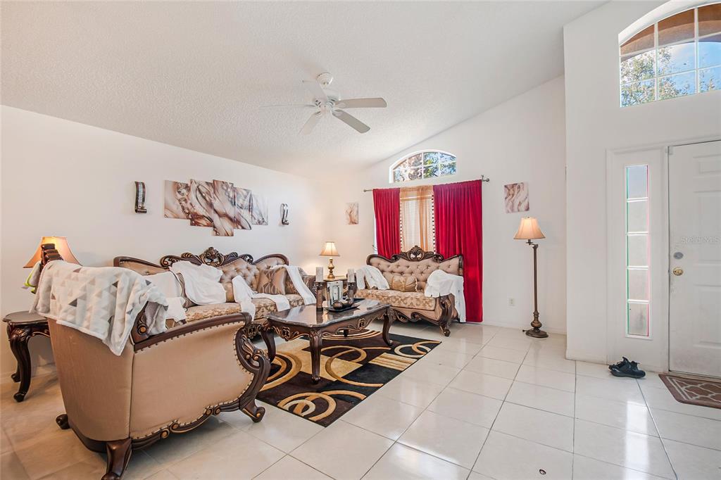 A living room with tile floors, ornate furniture, red curtains, and a vaulted ceiling — 1105 SEASONS BOULEVARD, KISSIMMEE, FL
