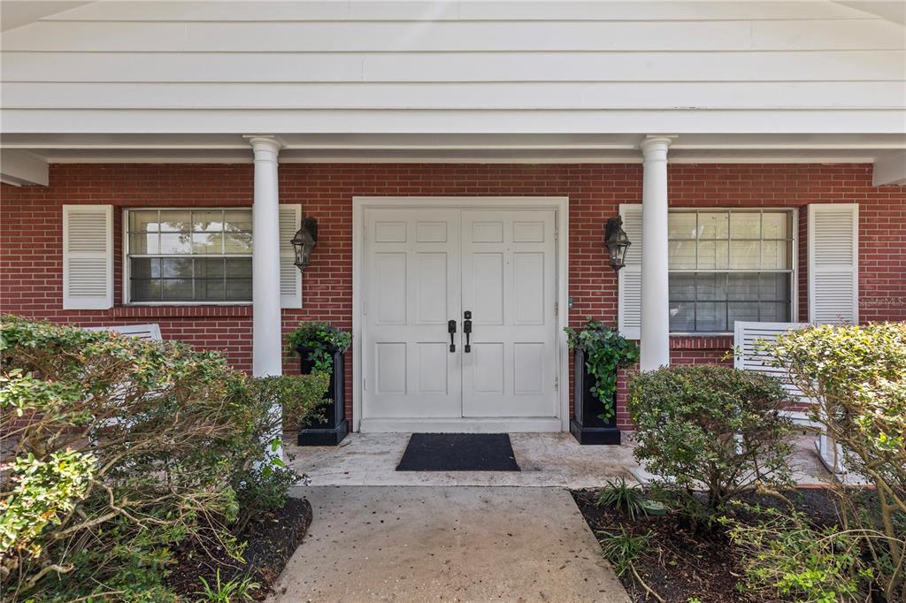 A brick house exterior features a white double front door, two columns, and white shutters — 6401 WINGFOOT CIRCLE, TAMPA, FL