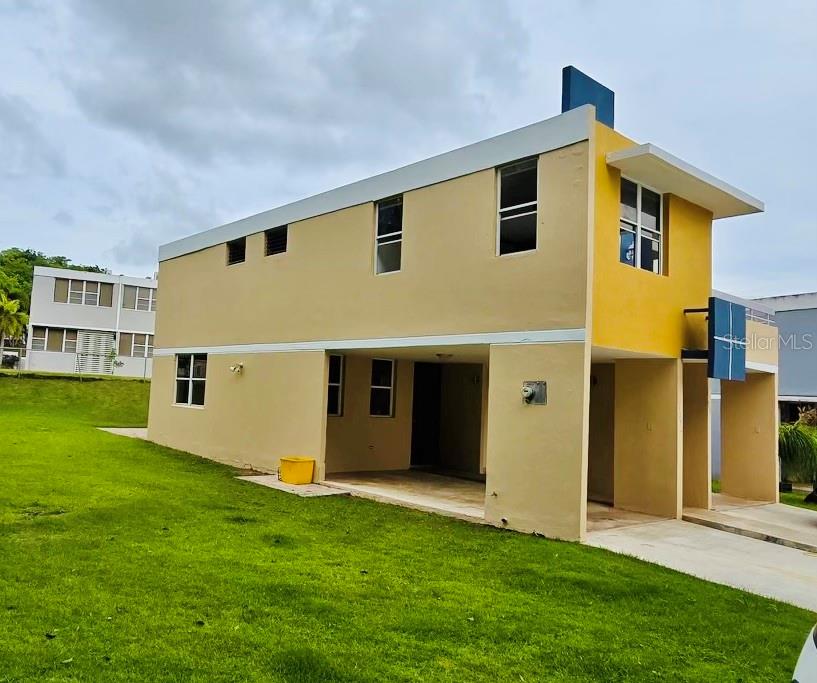 A two-story, tan-colored house with a carport and a grassy yard under a cloudy sky — D-1 FLAMINGO STREET, DORADO, PR