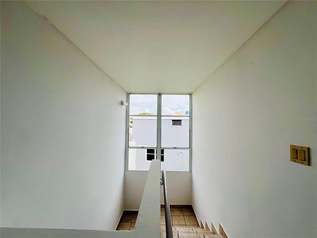 A staircase with a metal handrail leads down toward a large window overlooking buildings — D-1 FLAMINGO STREET, DORADO, PR