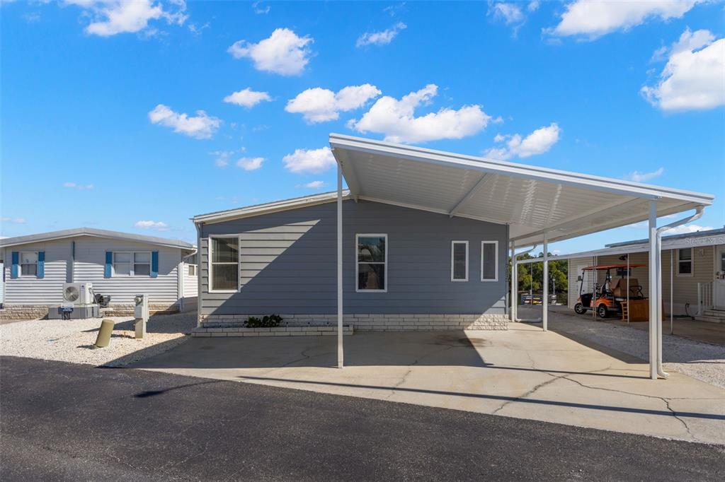 A grey manufactured home with a white carport and a concrete driveway under a blue sky — 7113 MOUNT PINEY ROAD NE UNIT 719, ST PETERSBURG, FL