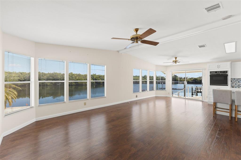 A spacious living area with dark wood floors, ceiling fans, and large windows overlooking water — 7113 MOUNT PINEY ROAD NE UNIT 719, ST PETERSBURG, FL
