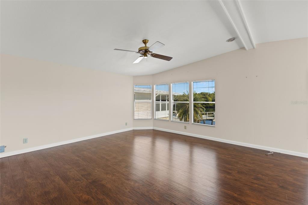 An empty room with dark wood flooring, a ceiling fan, and windows overlooking water — 7113 MOUNT PINEY ROAD NE UNIT 719, ST PETERSBURG, FL