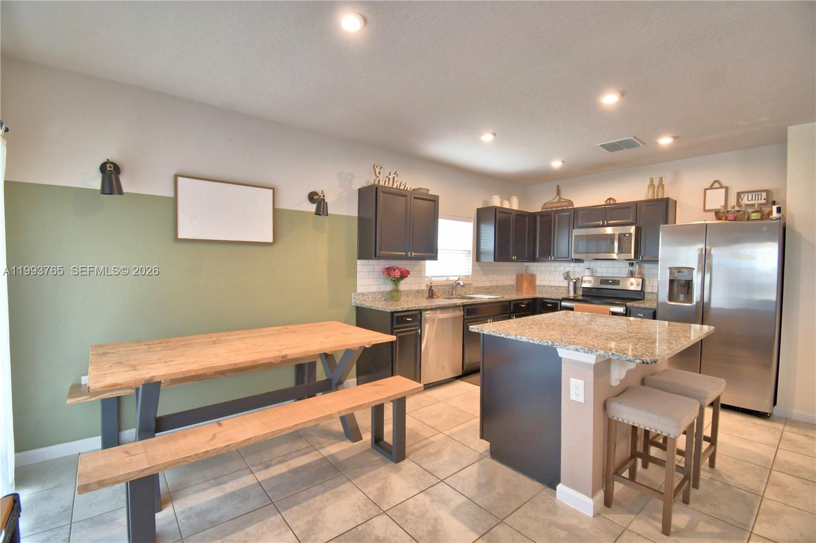 A kitchen features dark cabinets, granite countertops, a central island, and a wooden dining table — 542 Eagle Landing Blvd., Winter Haven FL 33880, WINTER HAVEN, FL
