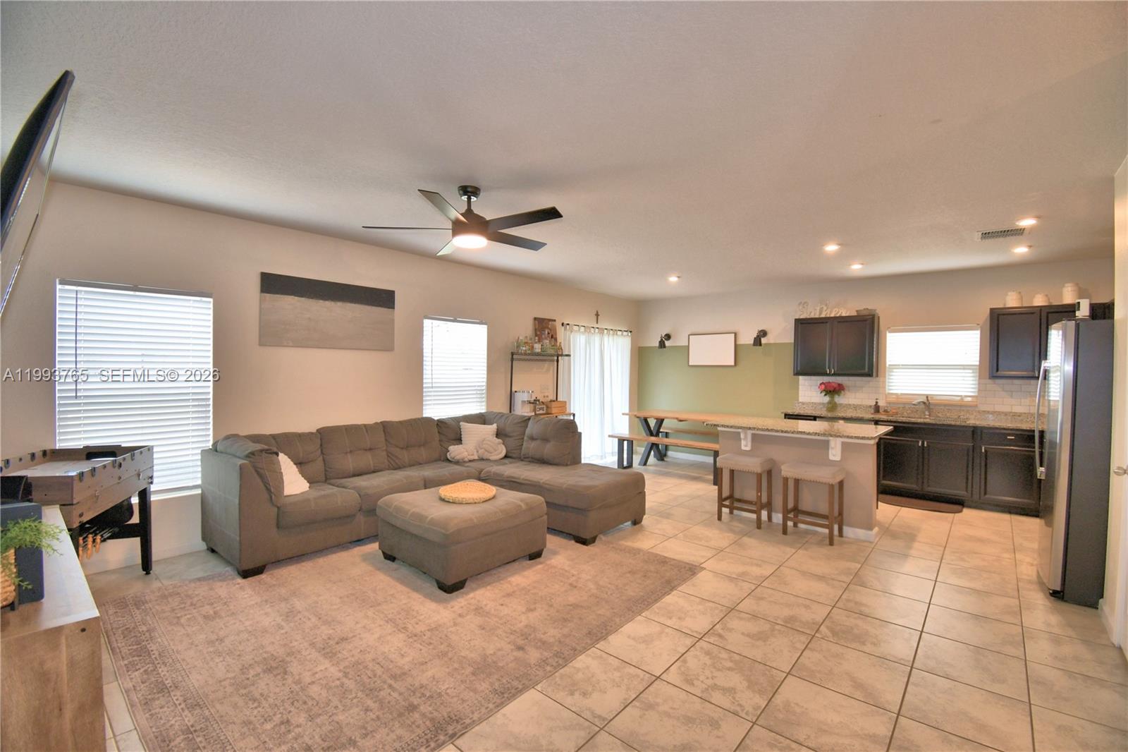 An open-concept living room and kitchen feature a gray sectional, tile flooring, and dark cabinetry — 542 Eagle Landing Blvd., Winter Haven FL 33880, WINTER HAVEN, FL