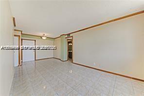 An empty room with light-colored tile flooring, beige walls, and wood trim — 2025 NE 164th St # 904, North Miami Beach FL 33162, NORTH MIAMI BEACH, FL
