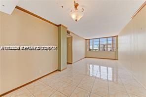 An empty living room features light-colored tile flooring, beige walls, and a large window — 2025 NE 164th St # 904, North Miami Beach FL 33162, NORTH MIAMI BEACH, FL