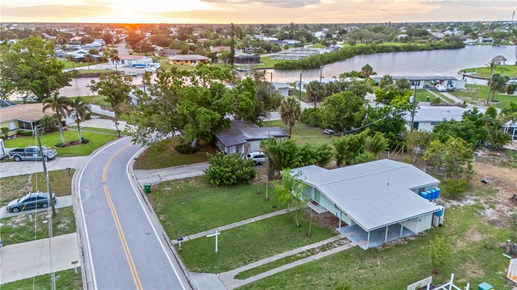 An aerial view shows a residential street with houses, palm trees, and a nearby canal — 180 PALMETTO CIRCLE NE, PORT CHARLOTTE, FL