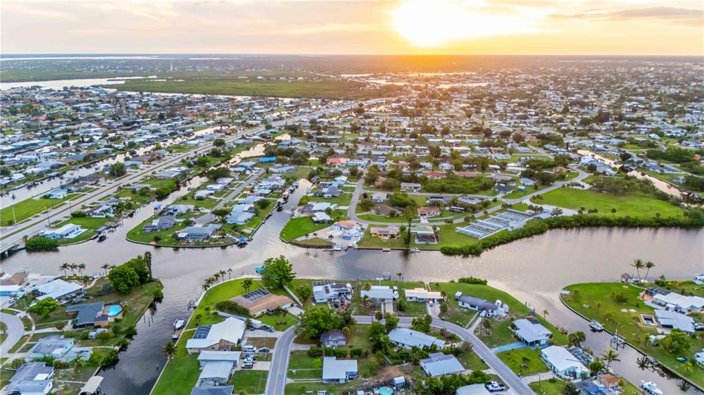 An aerial view of a residential neighborhood with houses situated along winding canals at sunset — 180 PALMETTO CIRCLE NE, PORT CHARLOTTE, FL