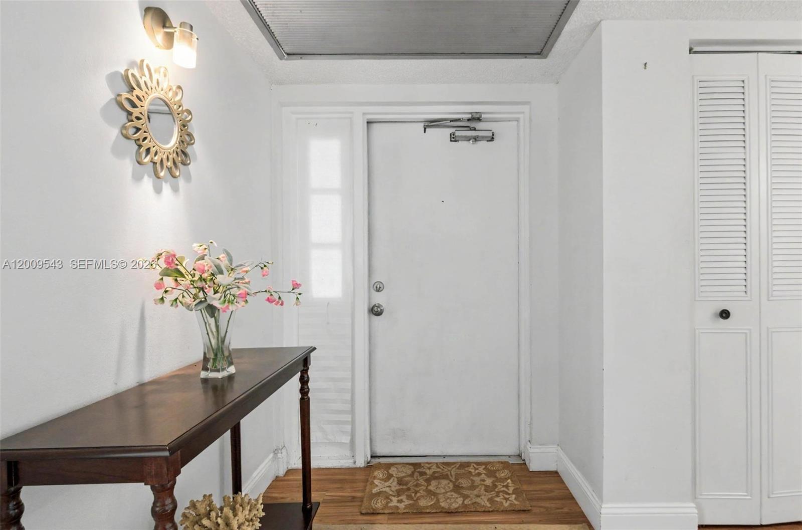 An entryway features a wooden console table, a decorative mirror, and a white door — 9340 Lagoon Pl # 110, Davie FL 33324, DAVIE, FL
