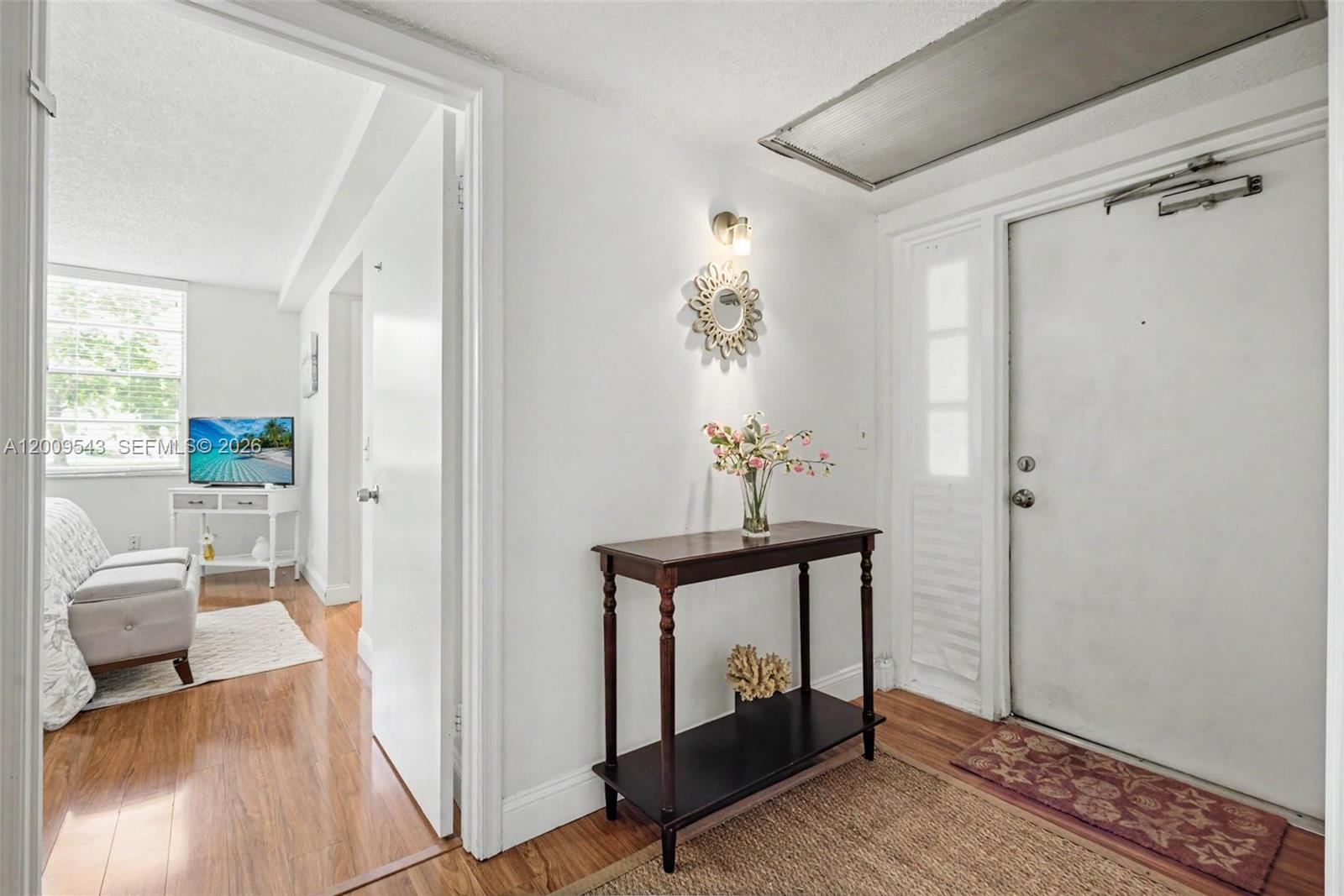 A white-walled entryway features a dark wood console table, a wall mirror, and wood flooring — 9340 Lagoon Pl # 110, Davie FL 33324, DAVIE, FL