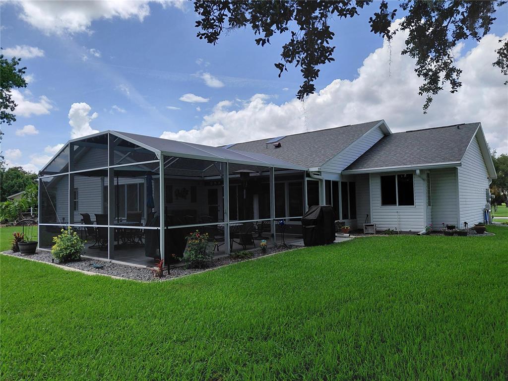 A white house with a screened-in patio and a large green lawn under a blue sky — 26010 NEWCOMBE CIRCLE, LEESBURG, FL