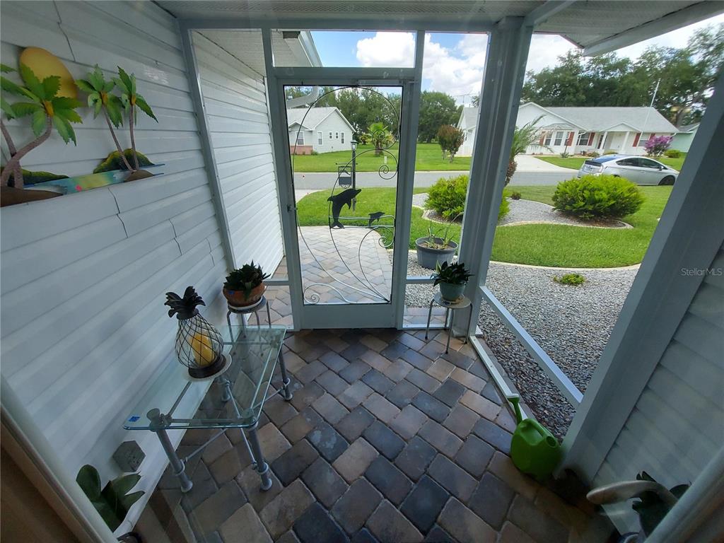 A screened-in porch features paver flooring, a decorative dolphin screen door, and outdoor decor — 26010 NEWCOMBE CIRCLE, LEESBURG, FL