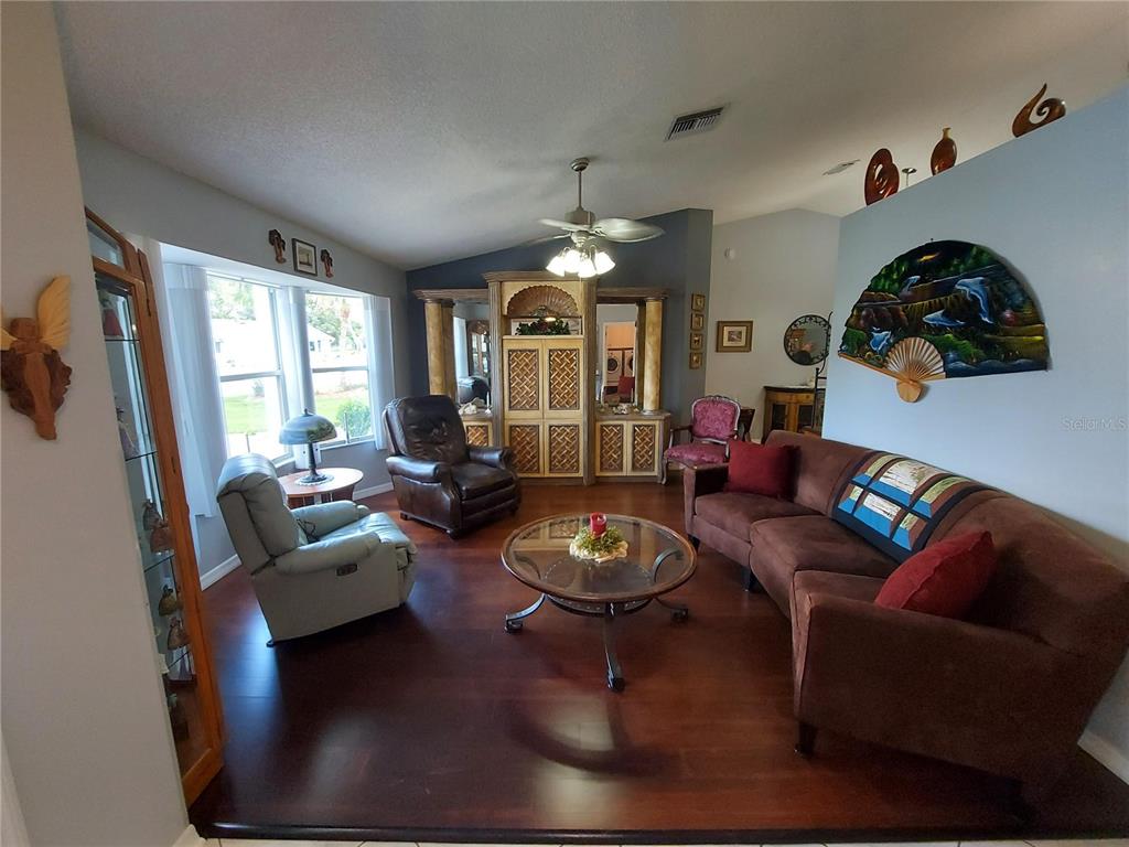 A living room features dark wood flooring, a brown sofa, armchairs, and a built-in cabinet — 26010 NEWCOMBE CIRCLE, LEESBURG, FL
