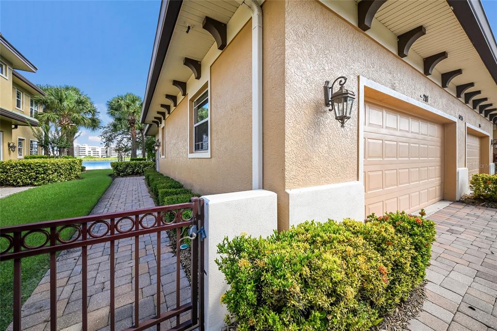 A side view of a tan stucco building with a garage, brick walkway, and gate — 6435 MOORINGS POINT CIRCLE UNIT 201, LAKEWOOD RANCH, FL