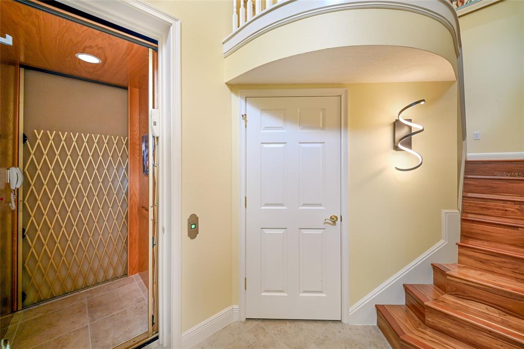 An indoor elevator with a metal gate sits beside a white door and wooden stairs — 6435 MOORINGS POINT CIRCLE UNIT 201, LAKEWOOD RANCH, FL