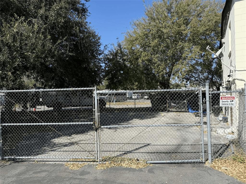 A chain-link fence encloses a paved parking area shaded by large trees — 5508 EDGEWATER DRIVE, ORLANDO, FL