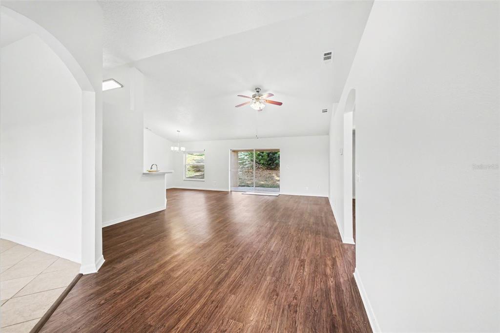 A spacious living area features white walls, wood-look flooring, a ceiling fan, and sliding doors — 10423 LAKE HASSON CIRCLE, CLERMONT, FL