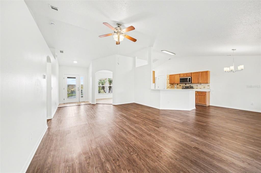 A spacious living room with wood-look flooring leads to an open kitchen with wooden cabinets — 10423 LAKE HASSON CIRCLE, CLERMONT, FL