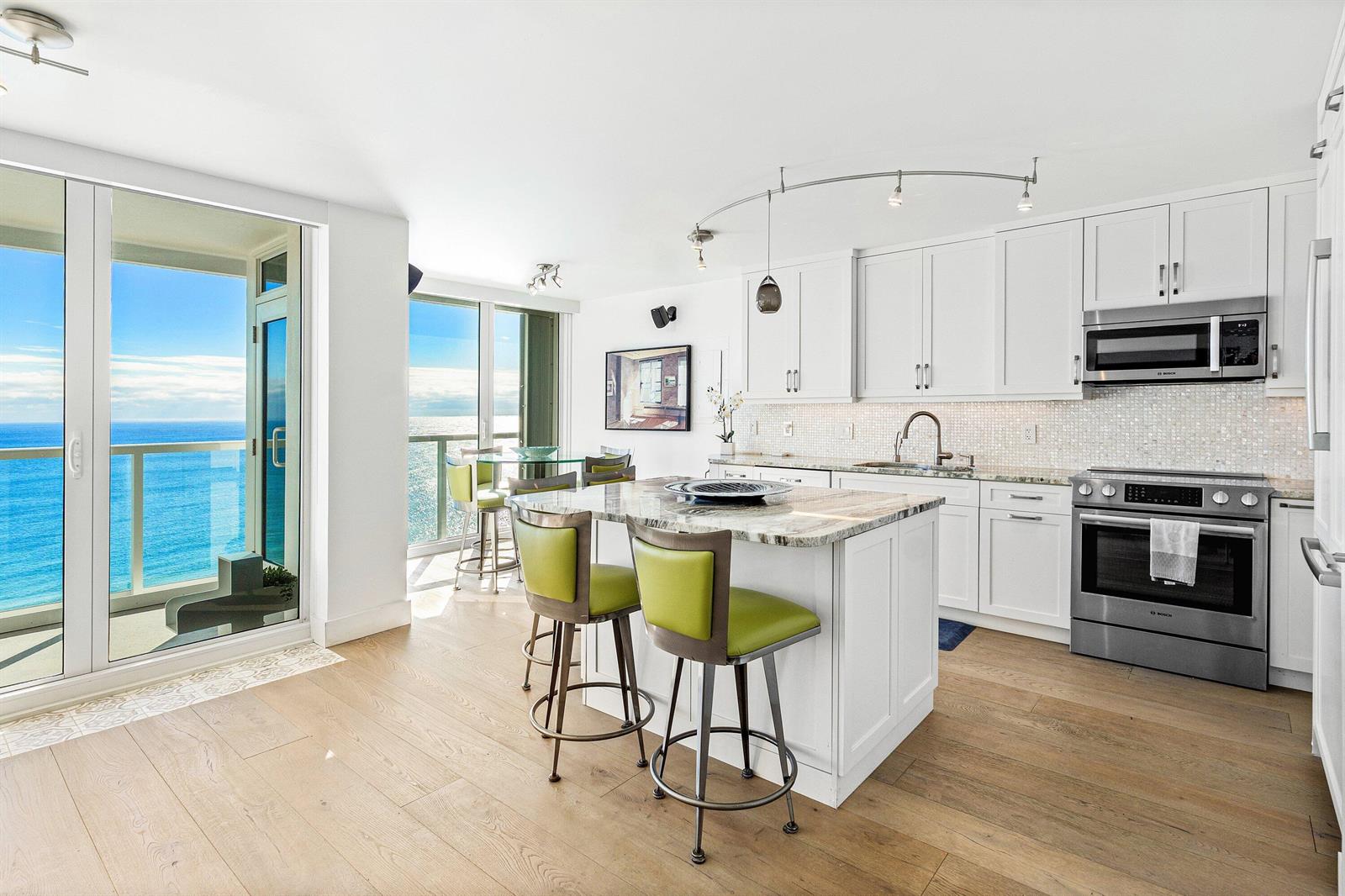 A bright kitchen features white cabinets, a stone island with green stools, and ocean views — 2800 S Ocean Boulevard # c, Boca Raton FL 33432, BOCA RATON, FL