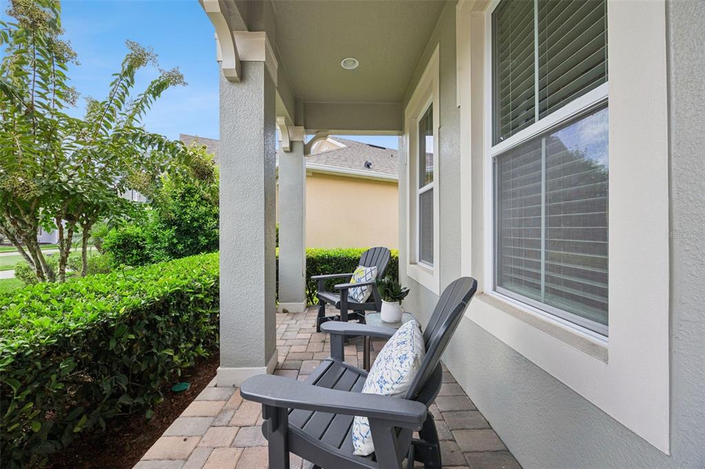 A covered front porch features paver flooring, two dark chairs, and a manicured hedge — 1048 WOOD DALE CIRCLE, OVIEDO, FL