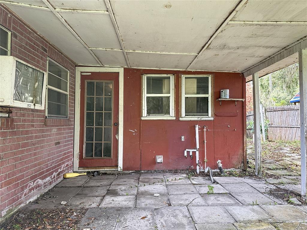 A covered patio with a brick wall, red siding, a glass-paneled door, and concrete pavers — 1880 CR 422, LAKE PANASOFFKEE, FL
