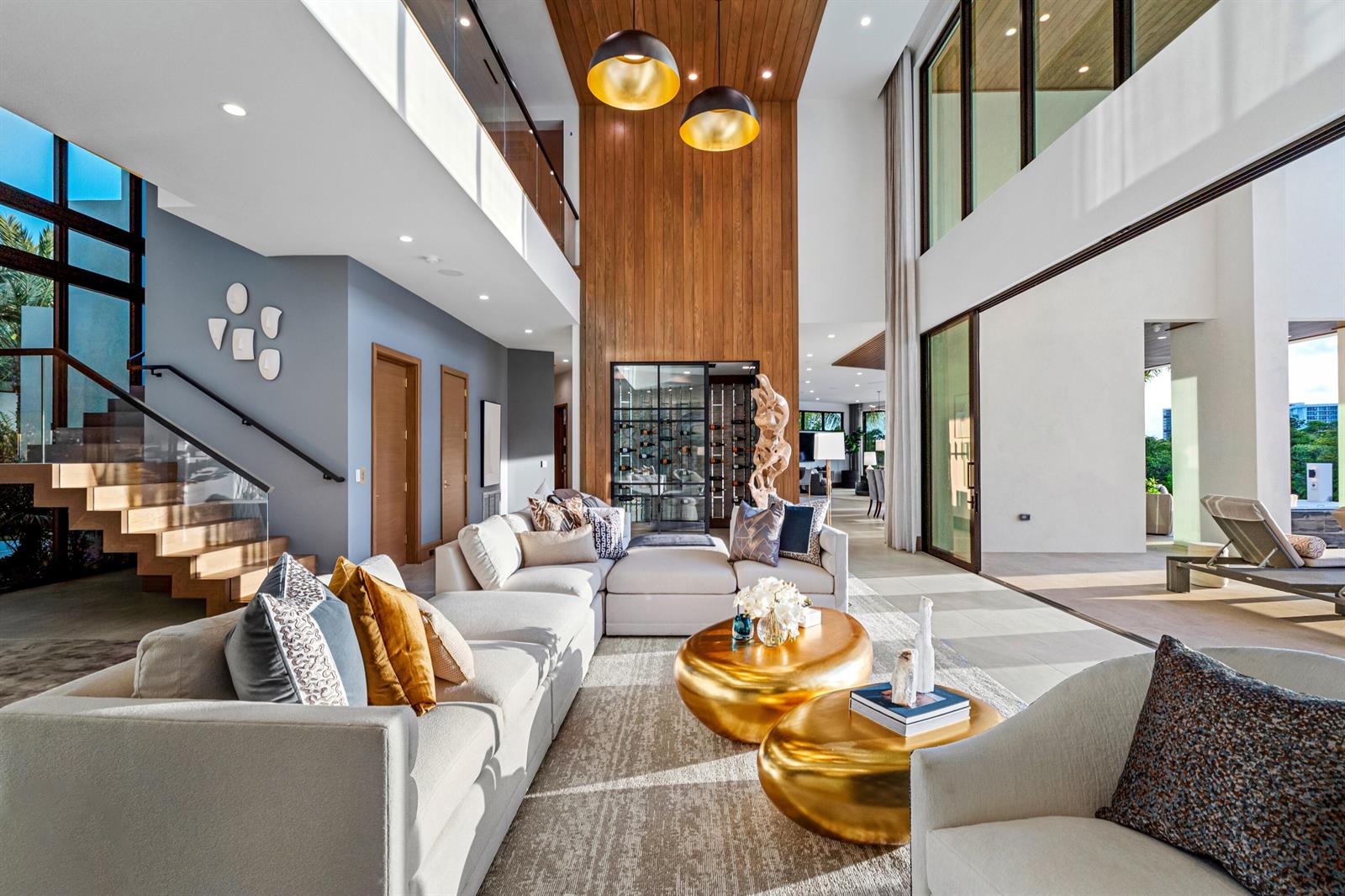 A modern living room features a double-height wood accent wall, gold coffee tables, and stairs — 4080 Ibis Point Circle, Boca Raton FL 33431, BOCA RATON, FL