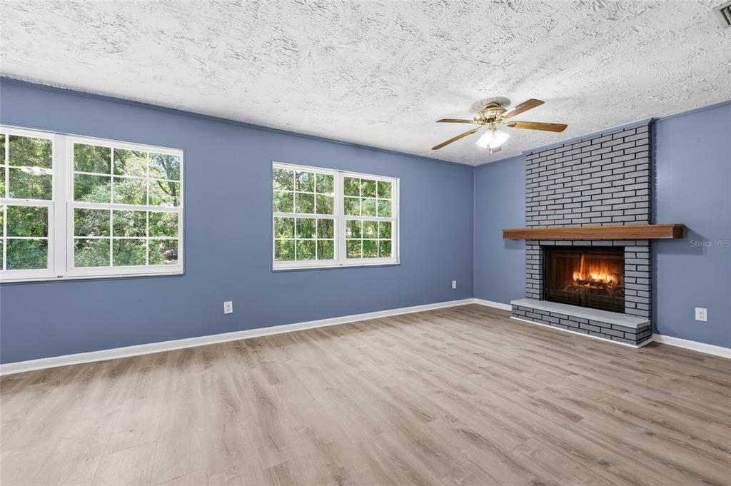 A living room with blue walls, light wood flooring, and a gray brick fireplace — 9350 NW 114TH STREET, CHIEFLAND, FL