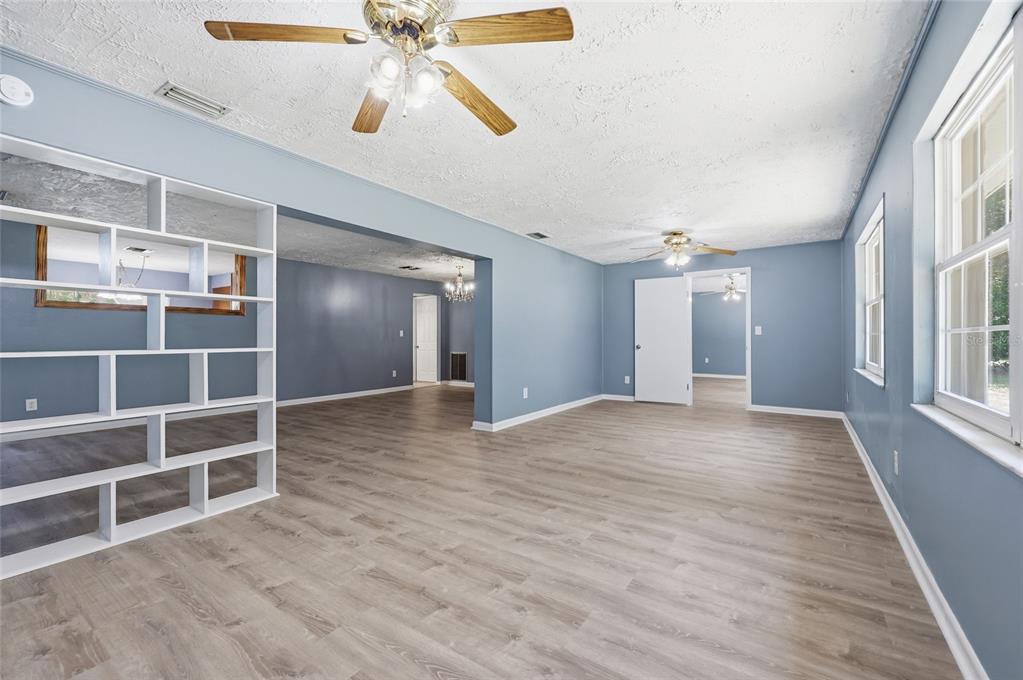 A living room with light blue walls, wood-look flooring, and a white open shelving unit — 9350 NW 114TH STREET, CHIEFLAND, FL