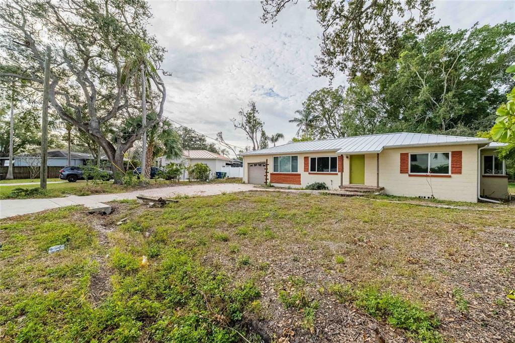 A single-story house with a light-colored exterior, a metal roof, and a large front yard — 6213 SANDERS DRIVE, TAMPA, FL
