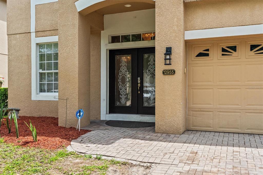 The exterior of a house features a tan stucco facade, a double front door, and a garage — 12955 MOSS PARK RIDGE DRIVE, ORLANDO, FL