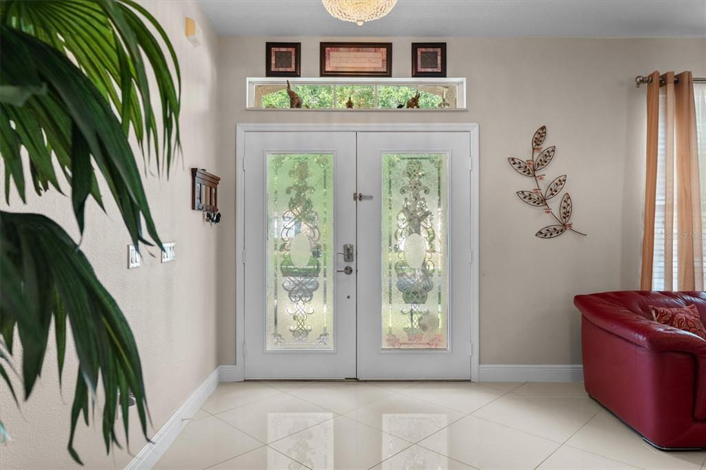 A bright entryway features double glass-paneled doors, tile flooring, and a decorative wall sculpture — 12955 MOSS PARK RIDGE DRIVE, ORLANDO, FL