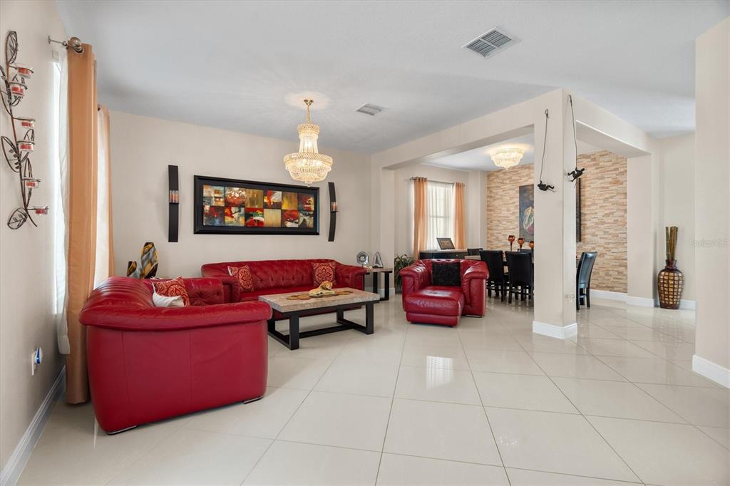 A living room with red leather furniture, a crystal chandelier, and tile flooring — 12955 MOSS PARK RIDGE DRIVE, ORLANDO, FL