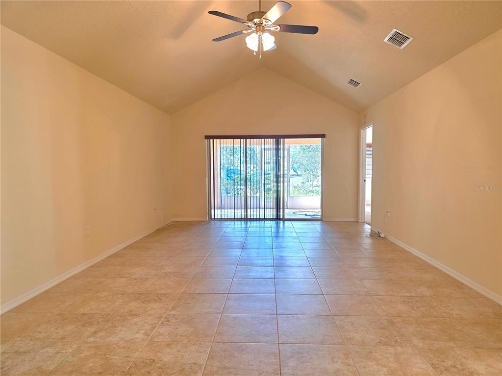 A living room with vaulted ceilings, tile flooring, a ceiling fan, and sliding glass doors — 4284 HIGH RIDGE AVENUE, SPRING HILL, FL