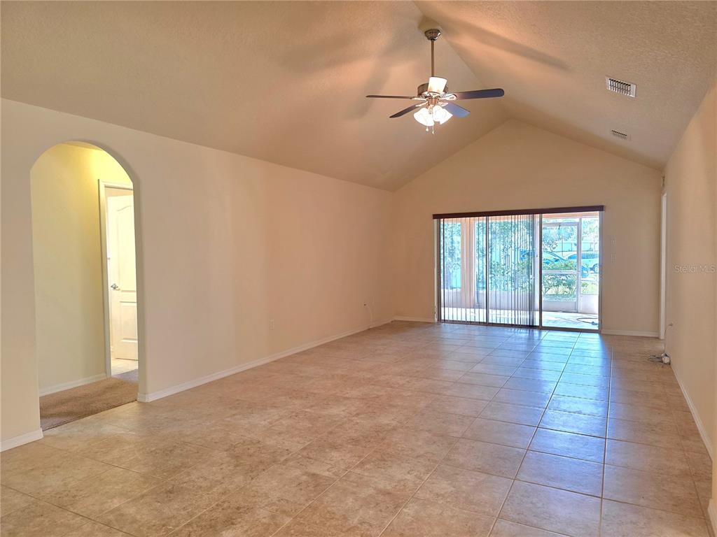 A spacious living room features vaulted ceilings, tile flooring, and sliding glass doors to a patio — 4284 HIGH RIDGE AVENUE, SPRING HILL, FL