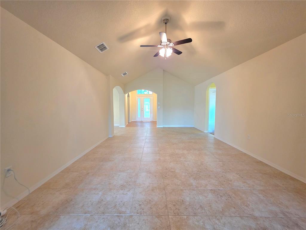 An empty room with beige tile flooring, vaulted ceilings, and a ceiling fan — 4284 HIGH RIDGE AVENUE, SPRING HILL, FL