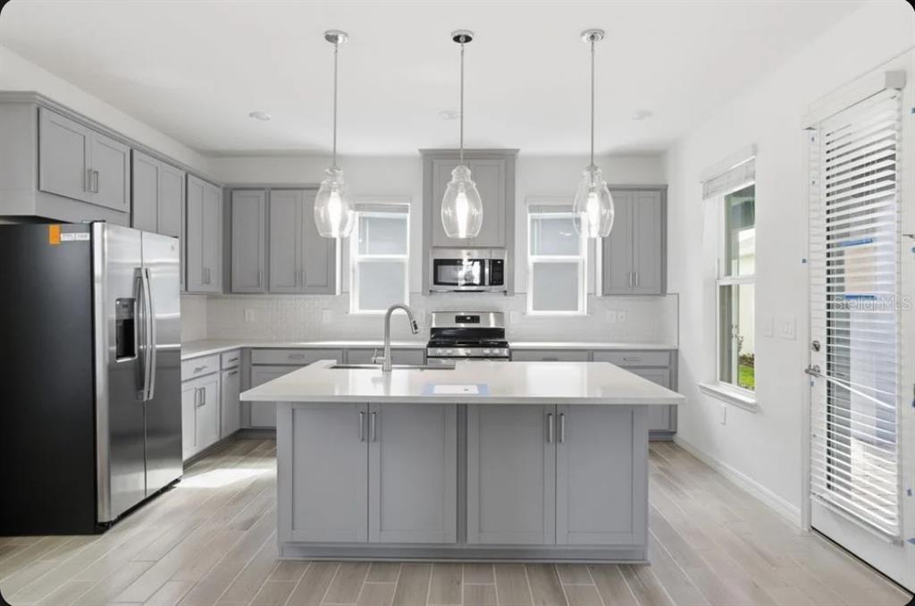 A modern kitchen features gray cabinets, a central island with a sink, and stainless appliances — 5169 FIRESTONE ALLEY, ST CLOUD, FL