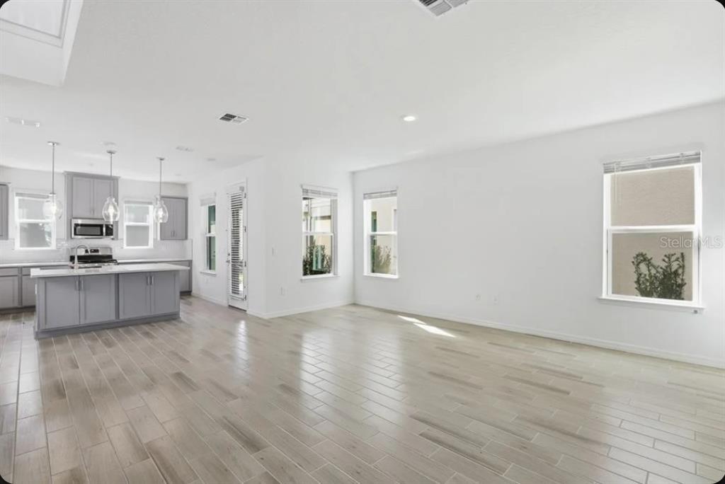 An open-concept kitchen with gray cabinets and an island overlooks a spacious living area — 5169 FIRESTONE ALLEY, ST CLOUD, FL