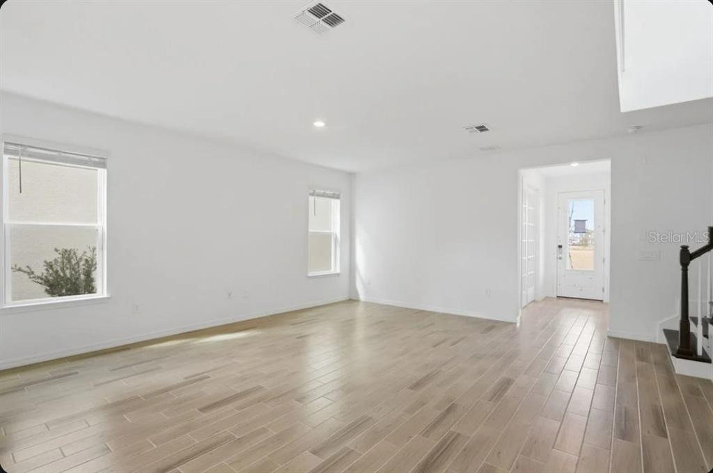 An empty living room with white walls, light wood-look tile flooring, and a front entryway — 5169 FIRESTONE ALLEY, ST CLOUD, FL