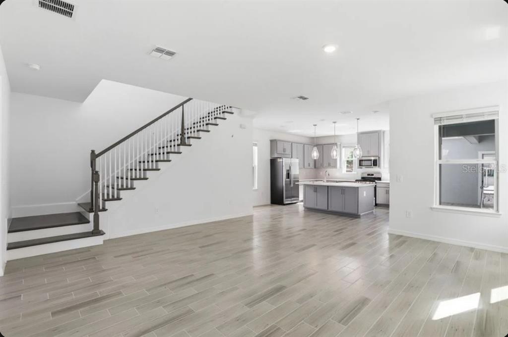 An open-concept living area features light wood-look tile flooring, a staircase, and a modern kitchen — 5169 FIRESTONE ALLEY, ST CLOUD, FL
