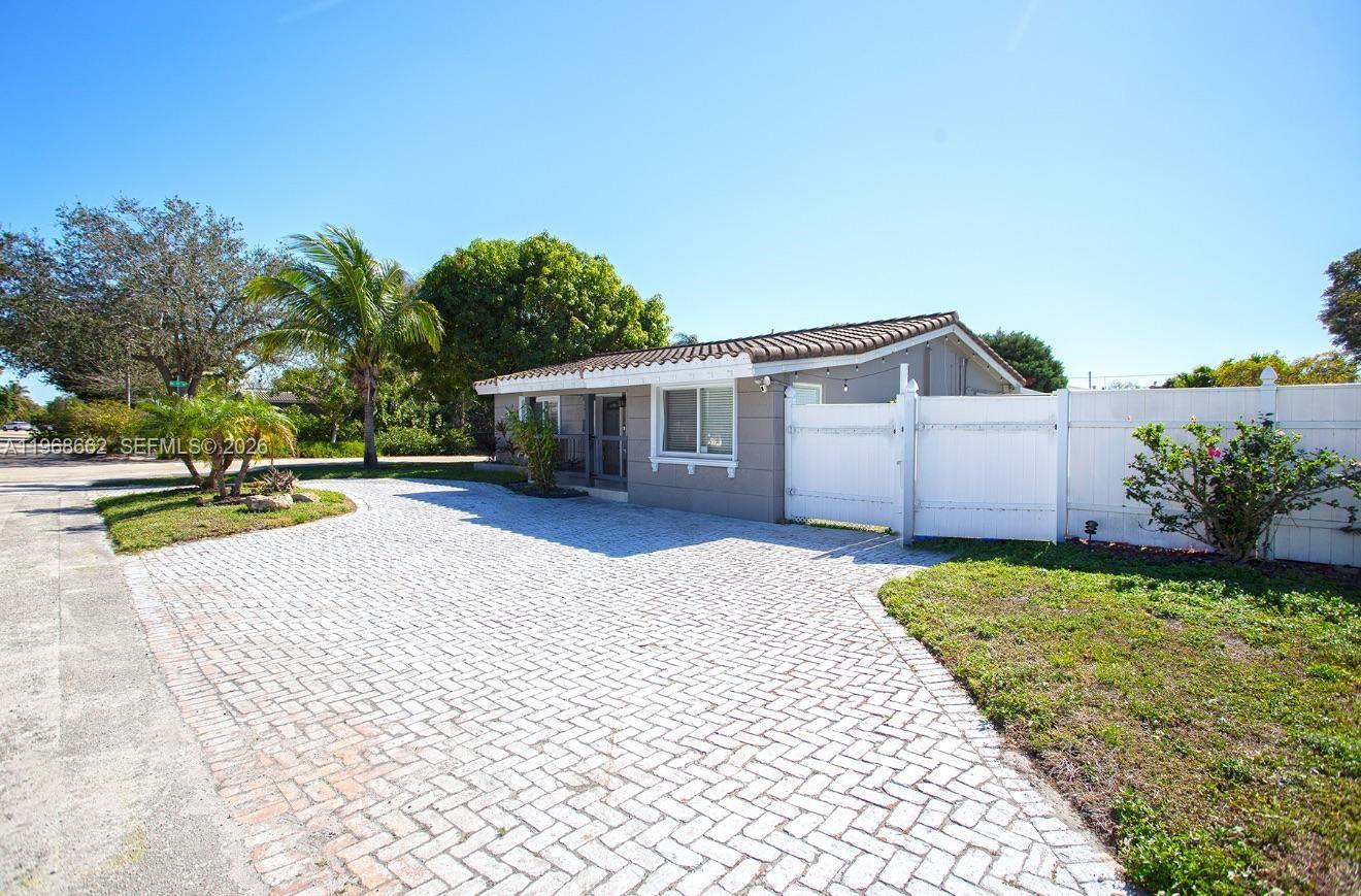A single-story house with a paved driveway and a white fence under a clear sky — 2450 NE 18th St, Pompano Beach FL 33062, POMPANO BEACH, FL