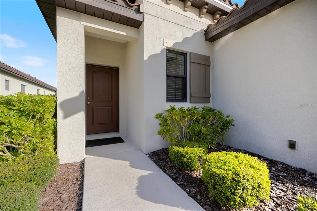 A brown front door is recessed into a white stucco house exterior with landscaping — 229 LIVORNO WAY, NOKOMIS, FL