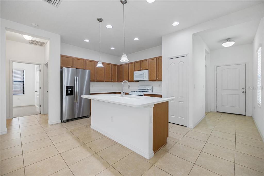 A kitchen with wood cabinets, stainless steel appliances, a white island, and tile flooring — 229 LIVORNO WAY, NOKOMIS, FL
